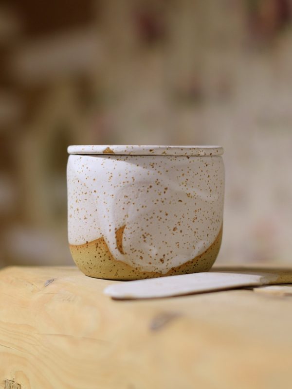 Biała, nakrapiana maselniczka wodna (French butter dish) z nożykiem do smarowania.